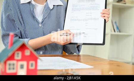 Weibliche Immobilienmaklerin zeigt und erklärt einem potenziellen Kunden im Büro den Mietvertrag. Zugeschnittenes Bild Stockfoto