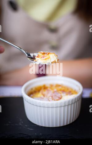 Eine junge Frau, die draußen in einem Restaurant Creme Brulee isst, ein Konzept von Urlaub und Sommer genießen. Vertikales Foto. Stockfoto