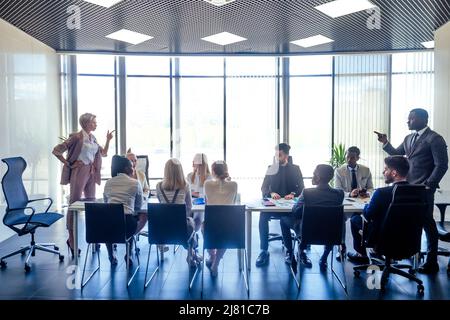 Verärgerte Geschäftsfrau argumentiert Mitarbeiter afroamerikanischer Mann schimpft Mitarbeiter für schlechte Ergebnisse oder diskutiert wichtige Anweisungen bei multirassischen Team Stockfoto