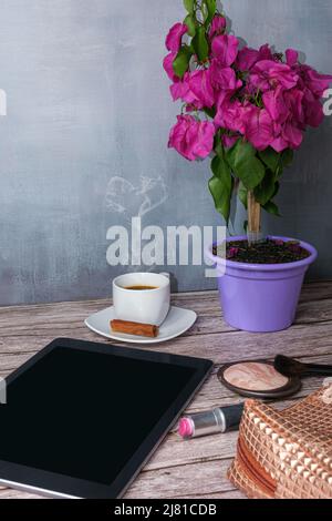 Tablet auf dem Tisch, umgeben von Kaffeetasse, Lippenstift und Make-up Bag Vertical photo. Stockfoto