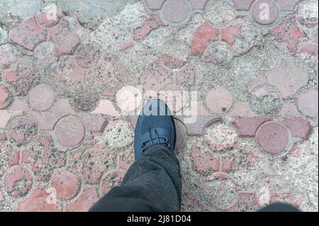Ein Blick auf meine Füße, die auf den alten Pflastersteinen laufen. Ein reifer Mann in grauen Hosen und blauen Sneakers geht die Stufen hinunter. Im Freien. Tagsüber. Selektiv f Stockfoto