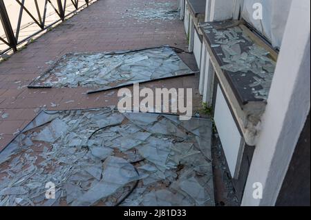 Die Fassade eines geschälten Gebäudes. Gebrochene Fenster liegen an der Wand. Die Nachwirkungen des Bombenangriffs auf eine ukrainische Stadt. Die russische Invasion der Ukraine Stockfoto