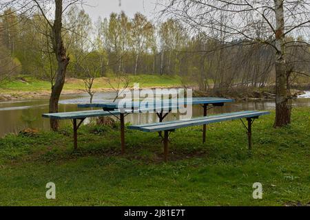 Holzpicknicktisch und zwei Bänke am Flussufer Stockfoto