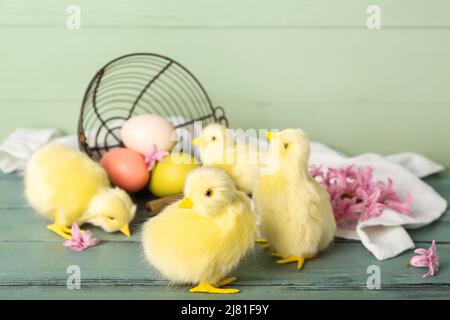 Niedliche Hühner, umgedrehtes Korb mit Ostereiern und Blumen auf Holztisch Stockfoto