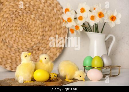 Niedliche Hühner, Ostereier und Blumen auf dem hellen Tisch Stockfoto