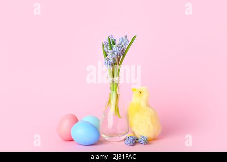 Niedliches gelbes Huhn, Vase mit Blumen und Ostereiern auf rosa Hintergrund Stockfoto