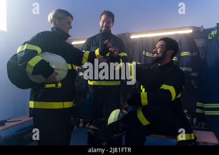 Glückliche Feuerwehrmänner Männer und Frauen, die sich nach dem Einsatz in der Feuerwehr unterhalten Stockfoto