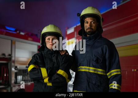 Glückliche Feuerwehrleute Mann und Frau nach der Aktion Blick auf Kamera mit Feuerwehrauto im Hintergrund Stockfoto