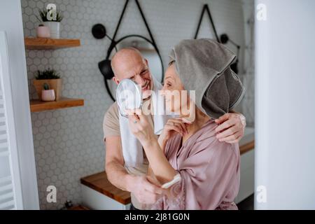Verliebtes Seniorenpaar im Badezimmer, der Spiegel ansah und lächelte, morgendliches Routinekonzept. Stockfoto
