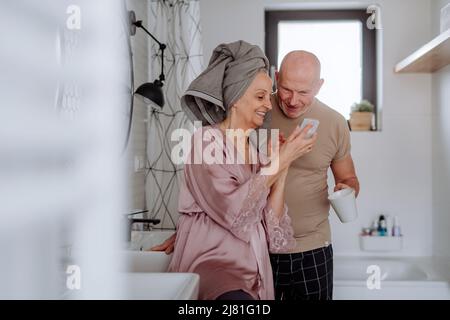 Verliebtes Seniorenpaar im Badezimmer, Smartphone, morgendliches Routinekonzept. Stockfoto