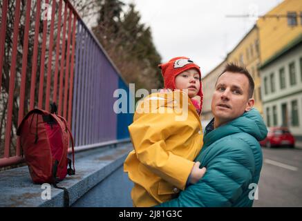 Vater bringt seine kleine Tochter mit Down-Syndrom zur Schule, draußen auf der Straße. Stockfoto