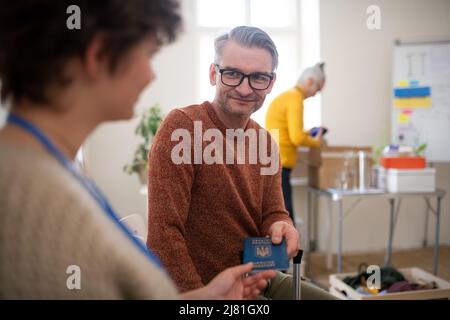 Junge Frau hilft dem ukrainischen Mann ehrenamtlich beim Ausfüllen von Formularen im Asylzentrum. Stockfoto