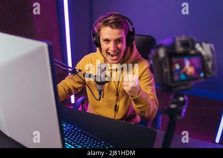 Der ausgesessene kaukasische Cyber-Sportler schießt Vlog, schreit fröhlich vor der Kamera, weil er das Spiel gewonnen hat, seinen Sieg feiert, macht ja Handbewegung. Pro Gamer Influencer hat Live-Video-Stream. Esport Stockfoto