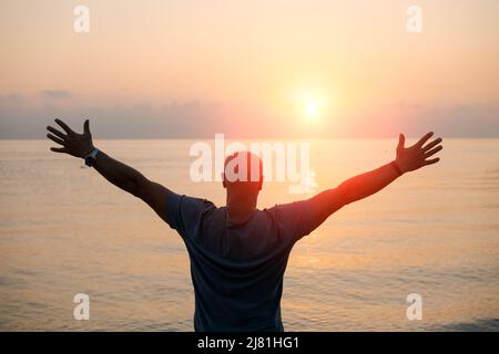 Silhouette Mann mit seinen Händen angehoben bei Sonnenuntergang am Strand Arme nach Seiten in Richtung der Sonne, Konzept für Religion, Anbetung, Gebet und Lob und Erfolg im Leben, Frieden und Ruhe in der Natur Stockfoto