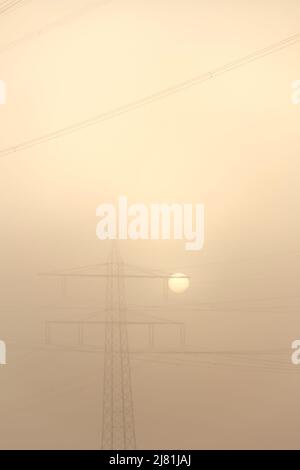 Sonne im Nebel hinter einem Strommast mit dem orangefarbenen Himmel im Hintergrund Stockfoto