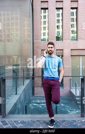 Junger bärtiger Mann, der auf der Straße steht, während er mit dem Handy spricht Stockfoto