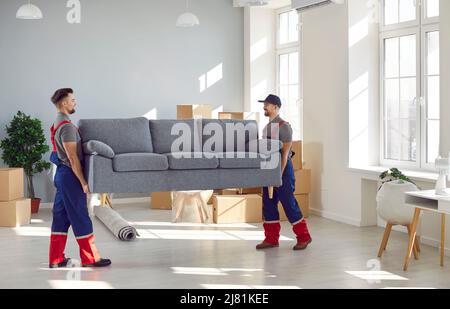 Männliche Lader nehmen das Sofa aus der Wohnung, während sie die Bestellung beim Umzugsdienst erfüllen. Stockfoto