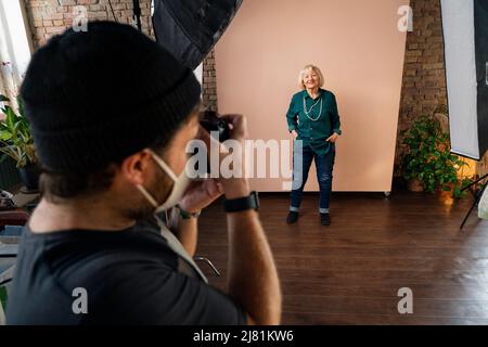 Junge Fotografin, die Bilder von älteren Frauen macht, hinter den Kulissen des Fotoshootings im Studio. Stockfoto