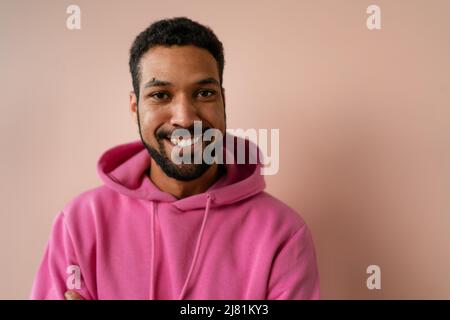Portrait eines jungen afroamerikanischen Mannes in pinkem Hoodie auf beigem Hintergrund. Stockfoto
