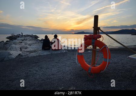 Wunderbarer Sonnenuntergang mit Lichtern, die sich im Meer und Himmel spiegeln, schafft eine magische Atmosphäre Stockfoto