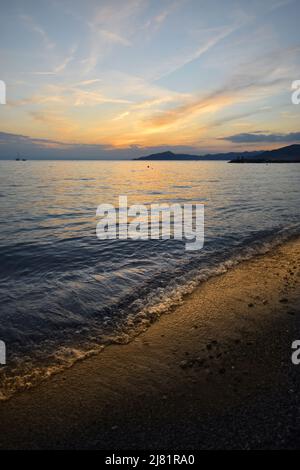 Wunderbarer Sonnenuntergang mit Lichtern, die sich im Meer und Himmel spiegeln, schafft eine magische Atmosphäre Stockfoto