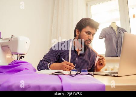 Schneiderei asiatische Mann Designer nähen Kleidung auf Nähmaschine neben Laptop Studio Arbeitsplatz Stockfoto