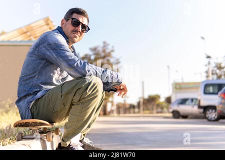 Erwachsener Mann sitzt auf seinem Skateboard und ruht sich aus Stockfoto