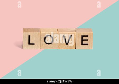 Holzwürfel mit dem Wort Liebe auf pastellrosa und blauem Hintergrund mit Kopierraum. Stockfoto