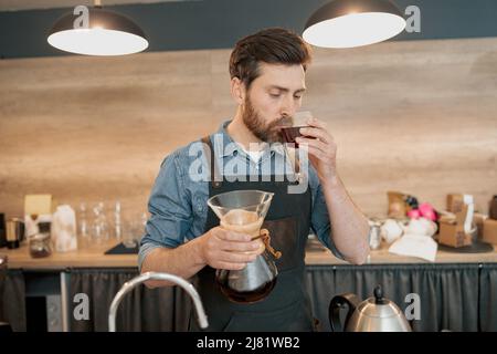 Der Barista verkostet einen frisch gebrühten Filterkaffee, der hinter dem Tresen steht Stockfoto