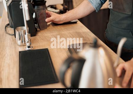 Der Barista installiert einen Behälter mit Kaffeebohnen in die Kaffeemaschine Stockfoto