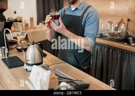 Der Barista hält ein Glas duftenden Filterkaffees in den Händen Stockfoto
