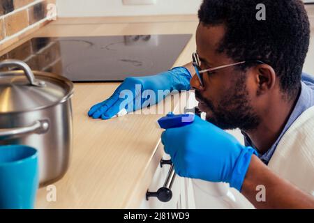 afrikanischer Mann, der die Dunstabzugshaube mit Kochplatte zu Hause putzt, Backsteinwand im Hintergrund Stockfoto