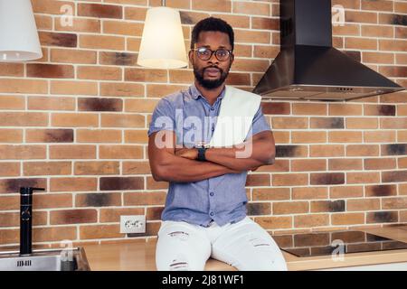 afrikanischer Mann, der die Dunstabzugshaube mit Kochplatte zu Hause putzt, Backsteinwand im Hintergrund Stockfoto