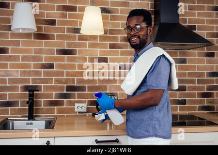 afrikanischer Mann, der die Dunstabzugshaube mit Kochplatte zu Hause putzt, Backsteinwand im Hintergrund Stockfoto