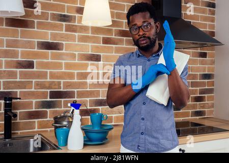 afrikanischer Mann, der die Dunstabzugshaube mit Kochplatte zu Hause putzt, Backsteinwand im Hintergrund Stockfoto