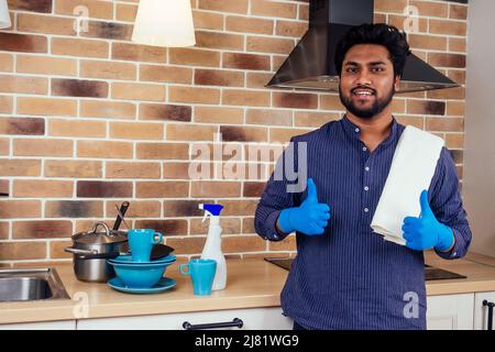 afrikanischer Mann, der zu Hause die Dunstabzugshaube putzt, Ziegelwand mit einem Berg ungewaschenen, schmutzigen Geschirrs in der Nähe des Waschbeckens Stockfoto