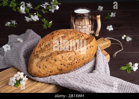 Frisches hausgemachtes Roggen-Getreidebrot mit Tonkrug Milch auf Holzschneidebrett. Gesundes Frühstück Stockfoto