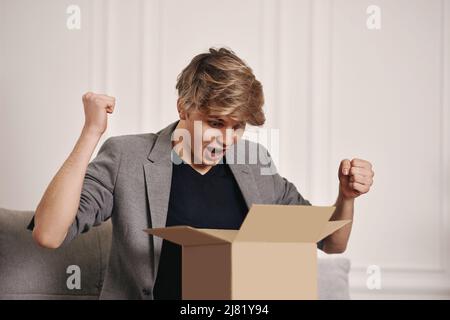 Mann auf der Couch sitzend und Pappkarton auspackend. Stockfoto