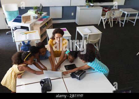 Junge kaukasische Lehrerin zeigt afroamerikanischen Grundschülerinnen im Unterricht einen Laptop Stockfoto