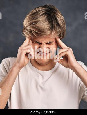 Junger hübscher Kerl, der auf grauem Hintergrund denkt. Stockfoto