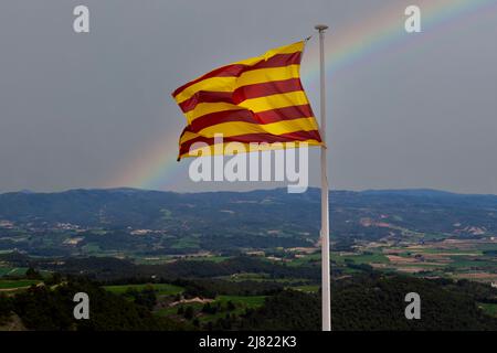 Flagge Kataloniens winkt in einer Landschaft und einem Regenbogen als Hintergrund Stockfoto