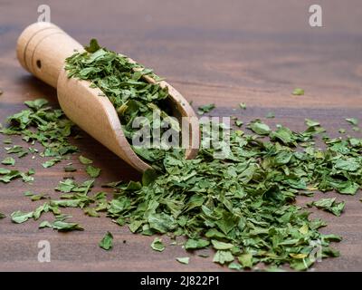 Antikes Holz Messlöffel gefüllt mit getrockneter Petersilie isoliert auf einem natürlichen Holztisch Stockfoto