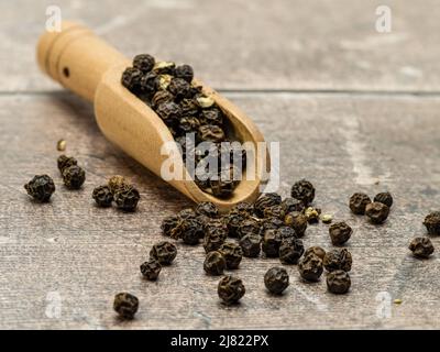 Holzlöffel mit ganzen schwarzen Pfefferkörnern isoliert auf weißem Hintergrund Stockfoto