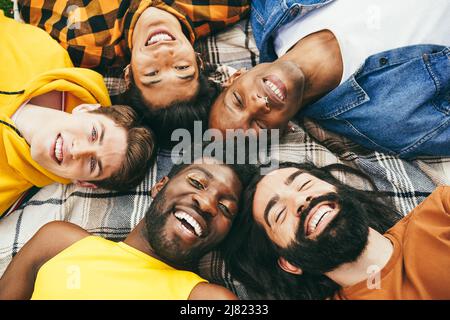 Glückliche verschiedene männliche Freunde, die Spaß haben, im Kreis im Freien zusammen zu liegen - Weiche Konzentration auf blonde Mann Stockfoto