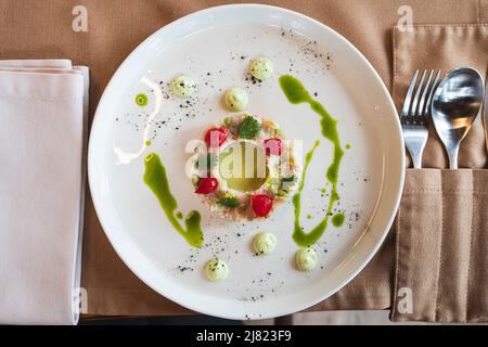 Der Salat aus verschiedenen Zutaten ist in Form eines Rings auf einem weißen Teller schön angerichtet. Stockfoto