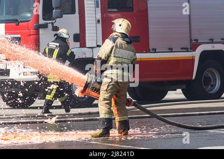 Firefighter - Feuerwehrmänner, die einen großen Brand verlöschen, stehen sie mit Schutzkleidung vor dem Hintergrund eines Feuerwehrfahrzeugs. Feuerwehrmann mit Exting Stockfoto