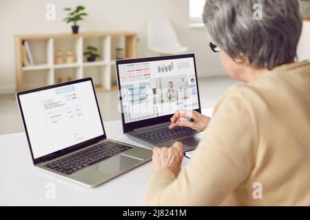 Frau, die Online-Unternehmensberatung und die Verwendung mehrerer Apps auf zwei Laptop-Computern Stockfoto