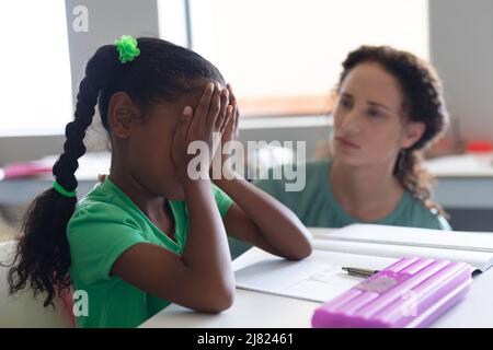 Kaukasische junge Lehrerin tröstet trauriges afroamerikanisches Grundmädchen mit verdecktem Gesicht Stockfoto