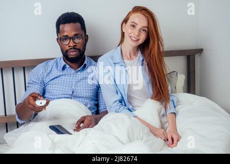 Ingwer Haar europäische weibliche und schöne afro afrikanischen Mann zusammen umarmt liegen im Schlafzimmer zu Hause gemütliche Wohnung Stockfoto