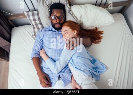 Ingwer Haar europäische weibliche und schöne afro afrikanischen Mann zusammen umarmt liegen im Schlafzimmer zu Hause gemütliche Wohnung Stockfoto